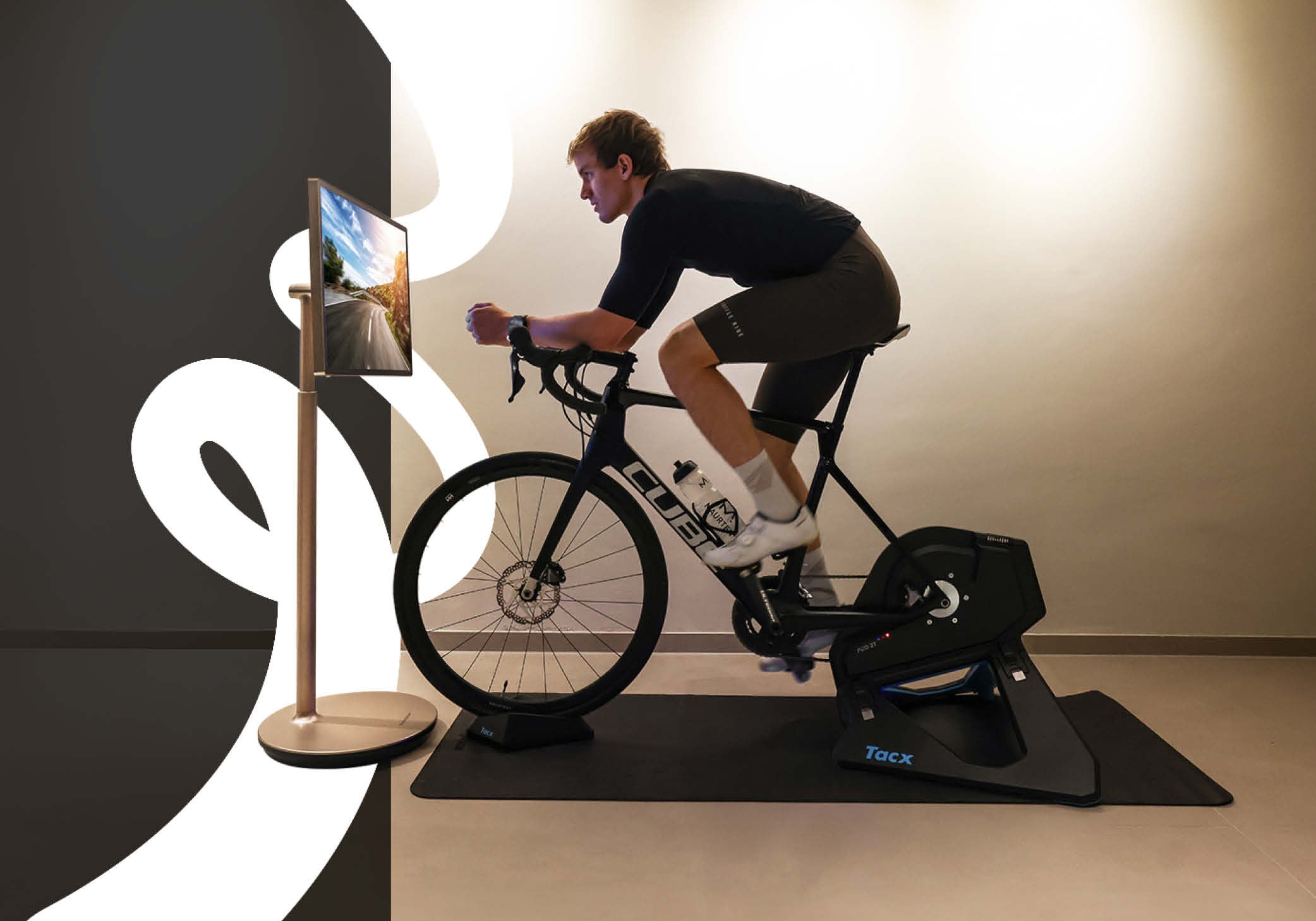 Indoor training session: Nico Rauchenwald pedals on a stationary bike, engaged with the Thomson Go Plus mobile TV in front of him.