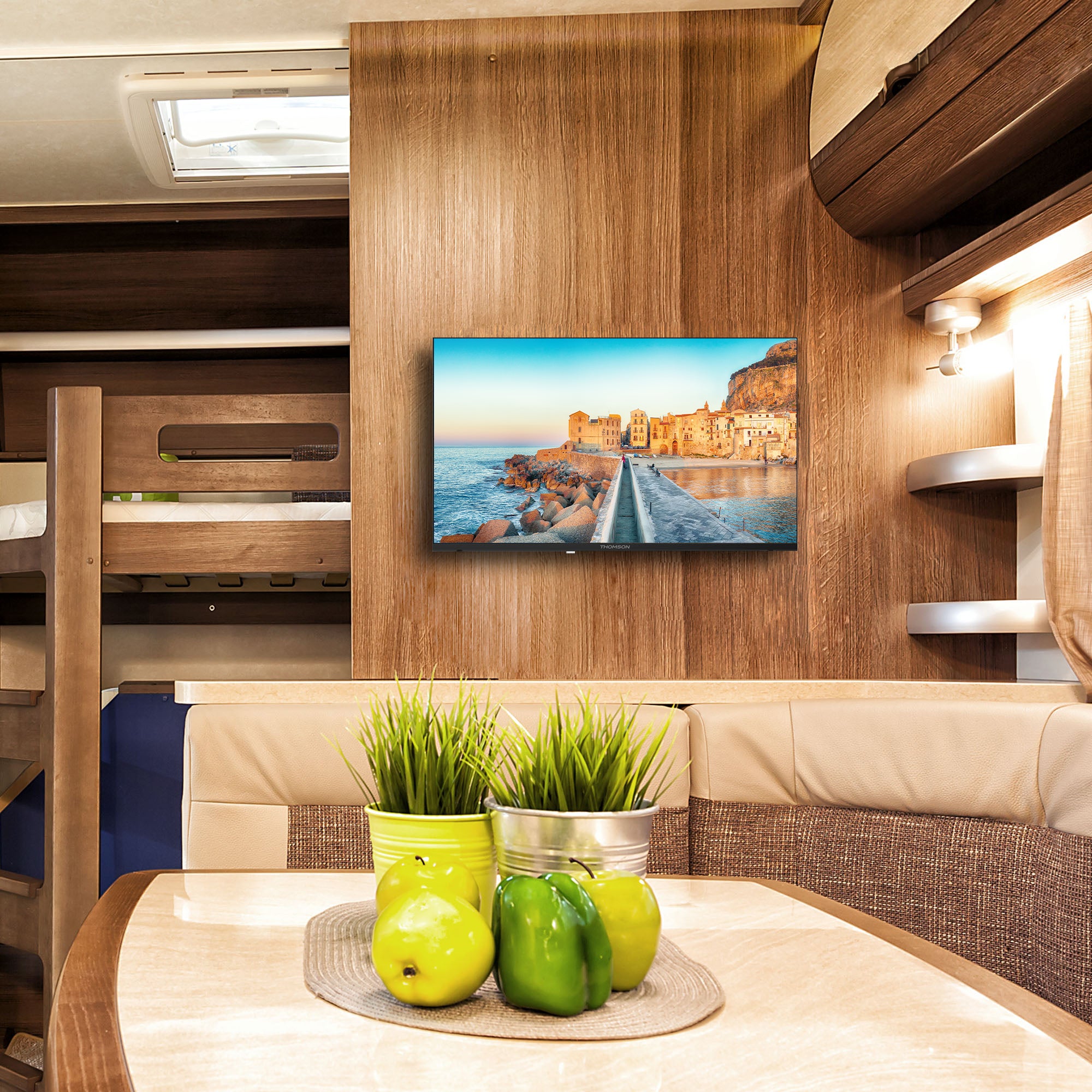 TV mounted on a wooden wall in a caravan interior with green apples and plants on a table.
