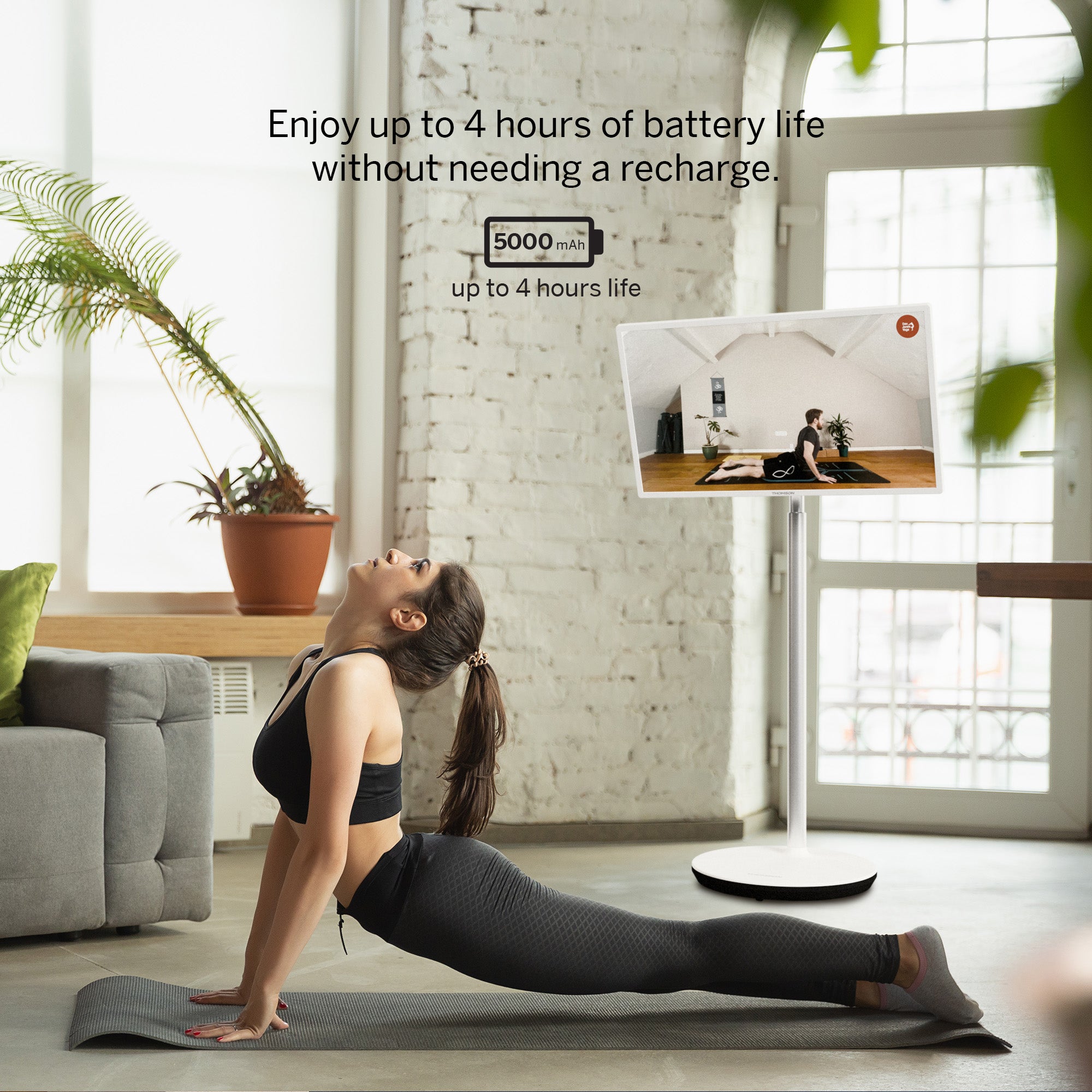 Woman exercising on a mat with a screen displaying a yoga session in the background.