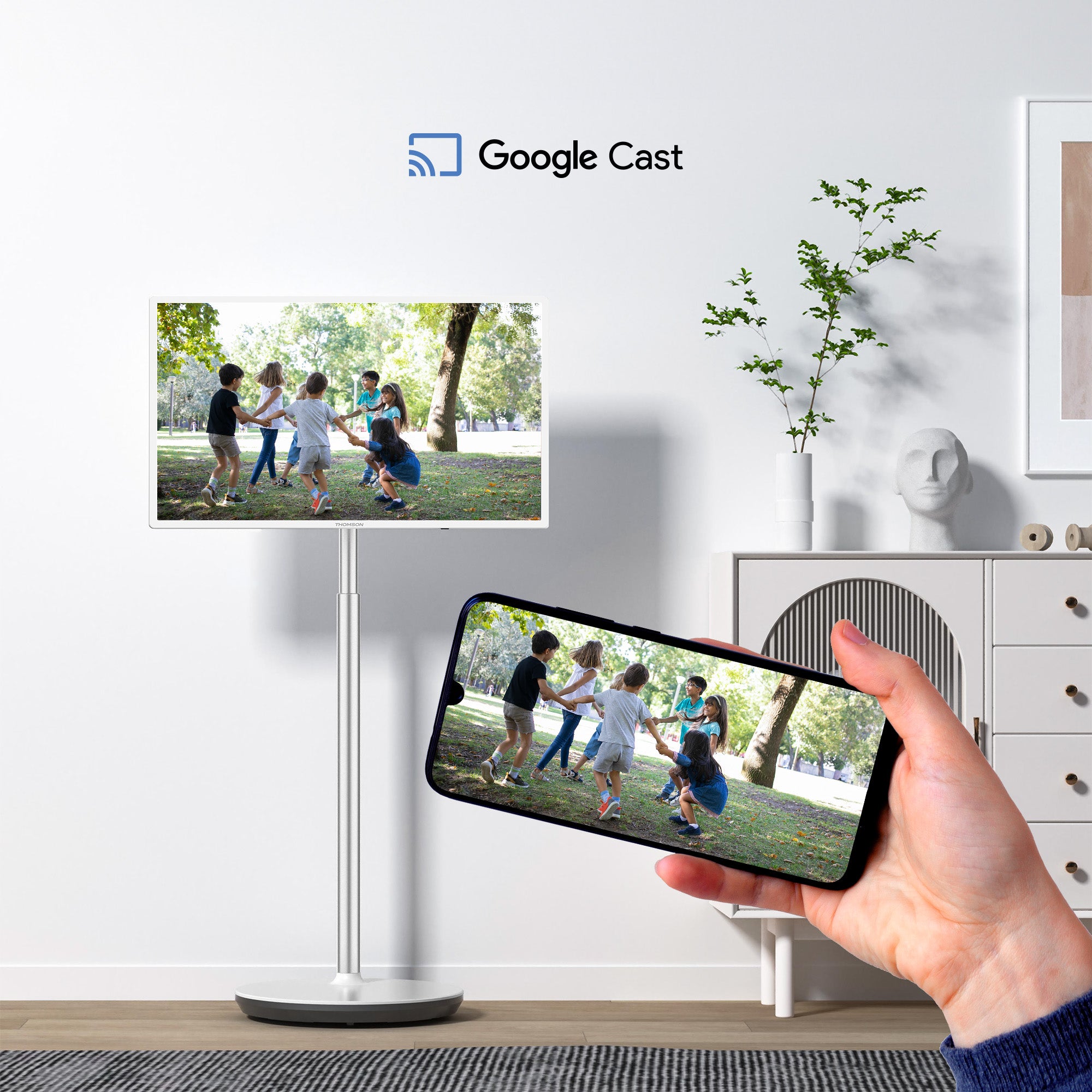 Hand holding a smartphone displaying a video of children playing, with a Google Cast logo in the corner.