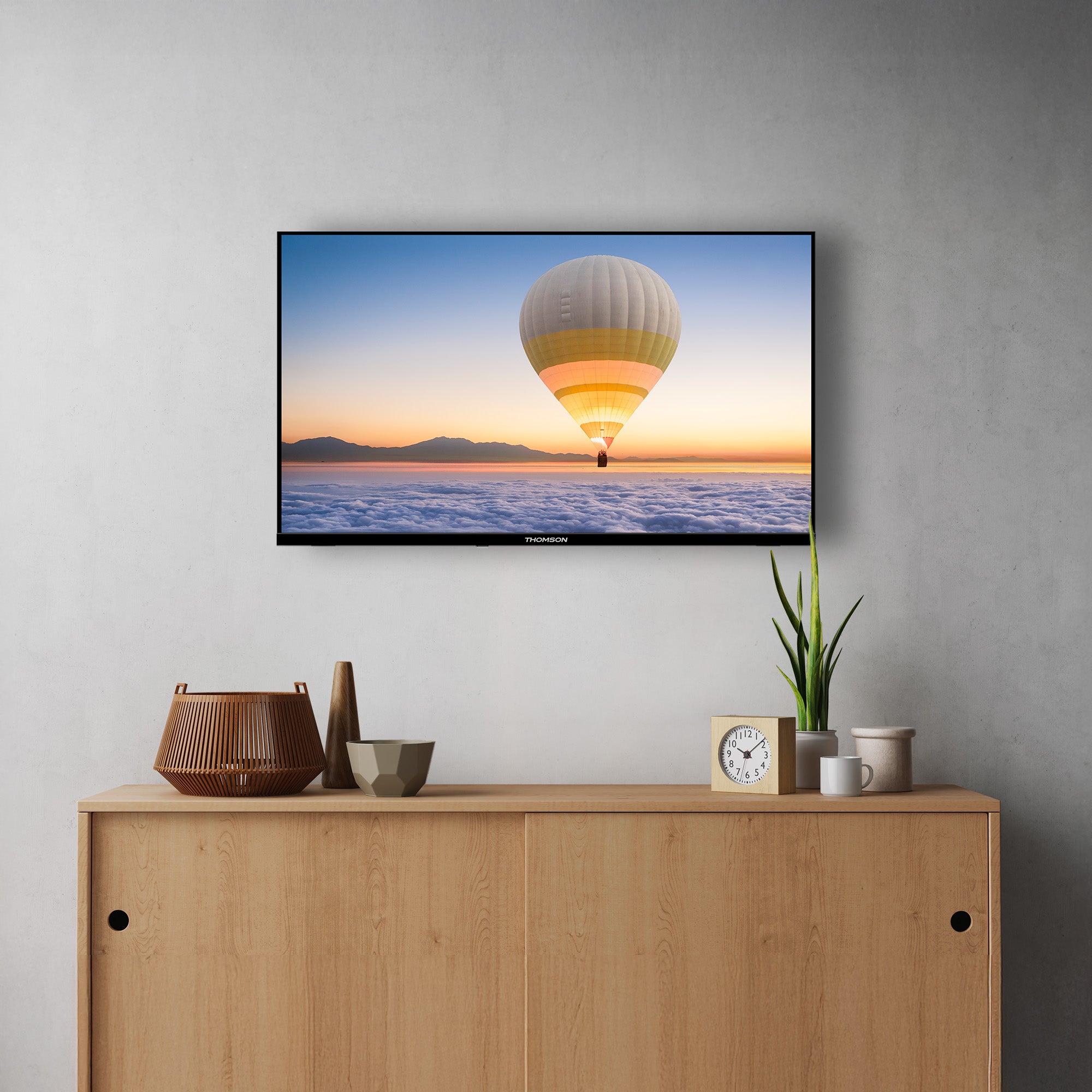TV mounted on a wall displaying a hot air balloon over water, below a wooden cabinet with decorative items.