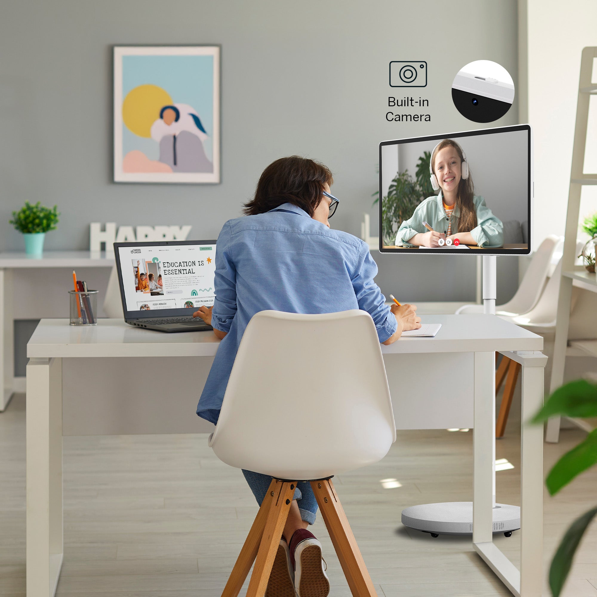Person sitting at a desk with a laptop, interacting with another person on a screen.