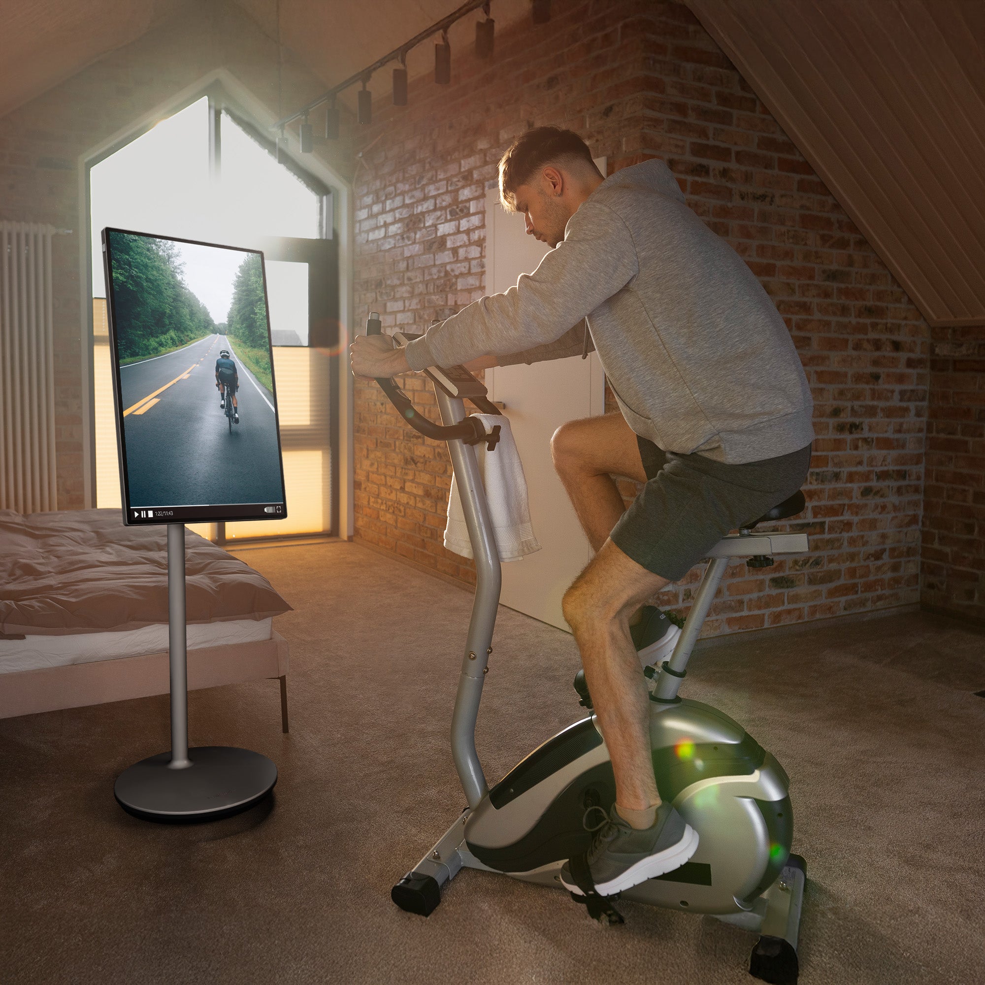 Man exercising on a stationary bike in a room with a portable screen displaying a cycling scene.
