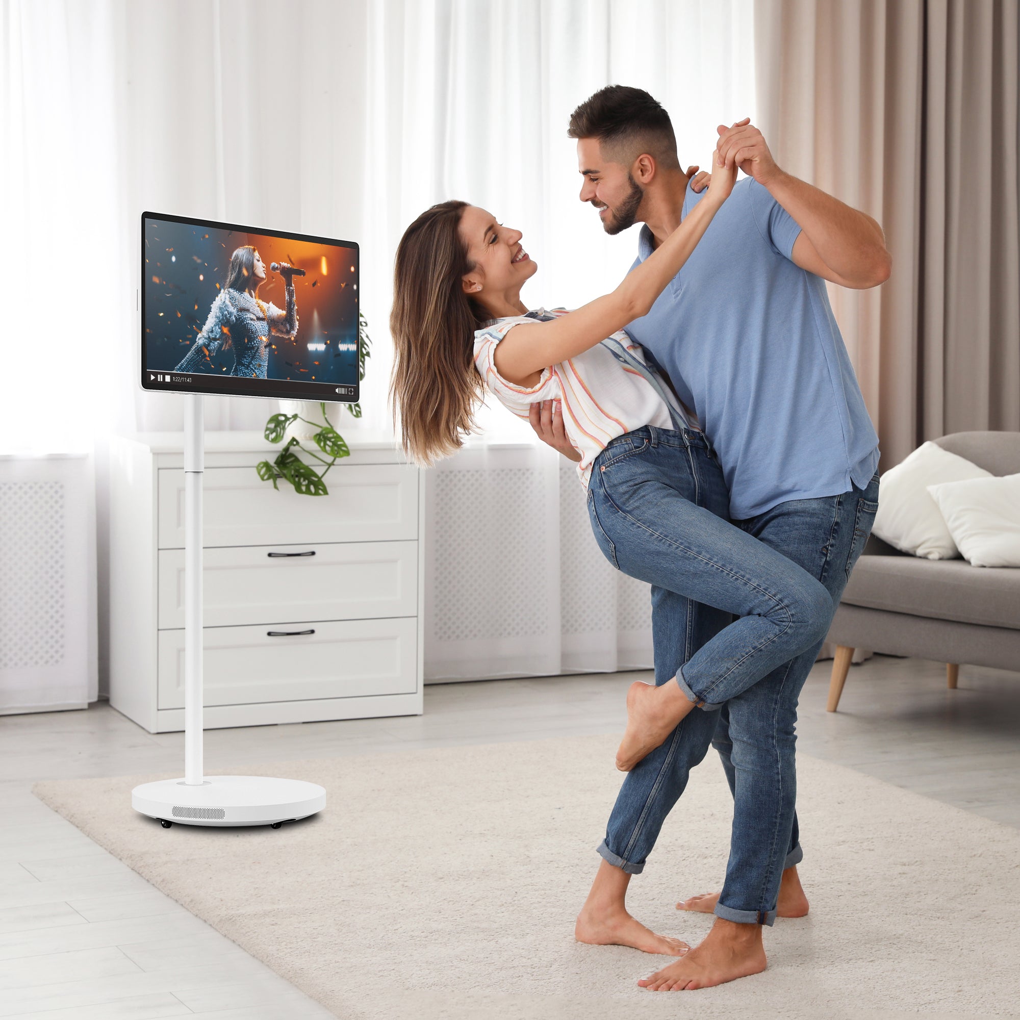 Dancing couple in a bright livingroom  with a portable display on wheels in the background.